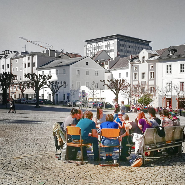 Menschen sitzen im Sesselkreis auf öffentlichem Platz